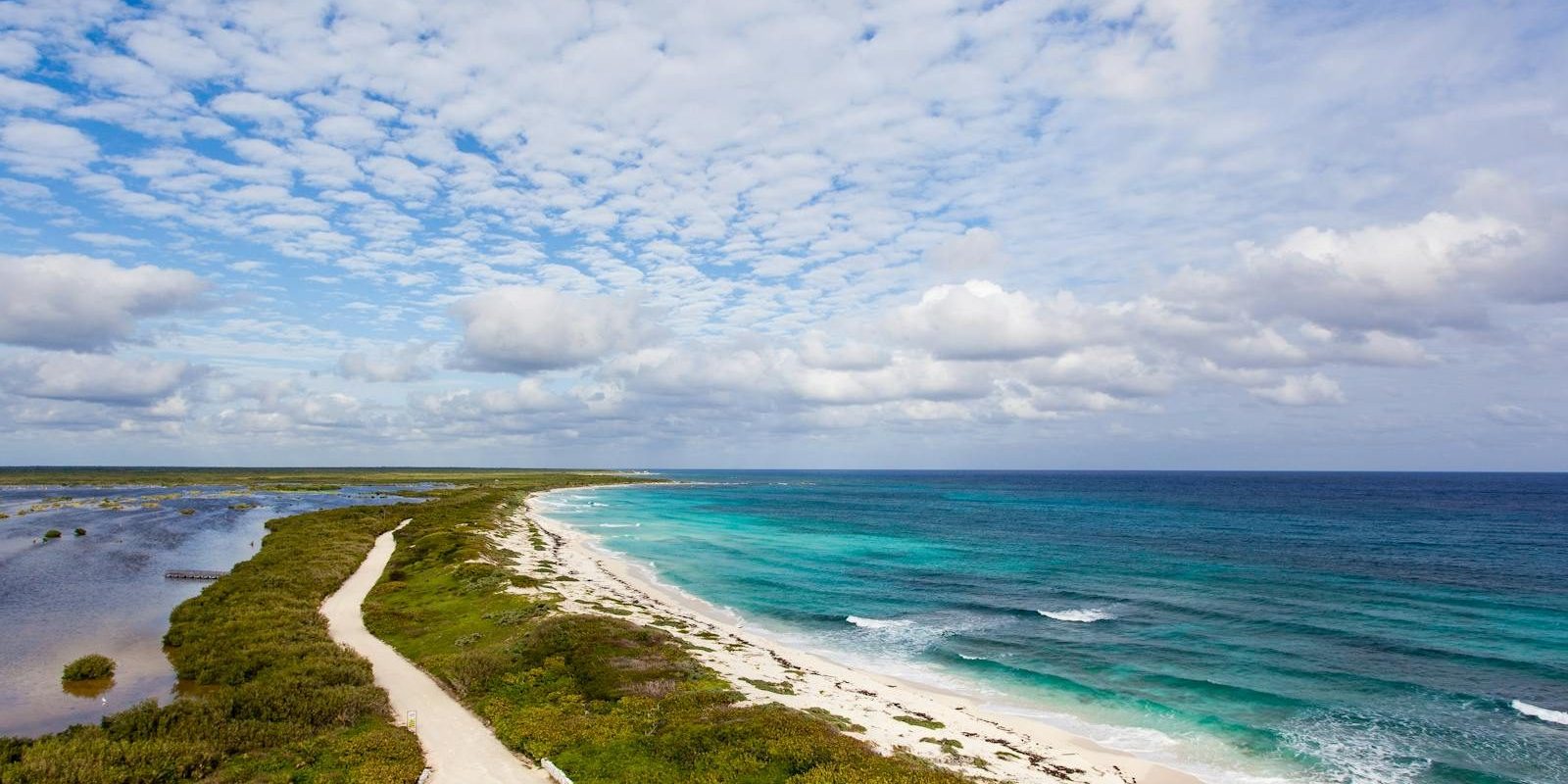 A serene aerial view of a white sandy beach, lush greenery, and the azure ocean under a cloud-filled sky.