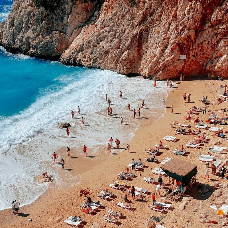 Aerial shot of people enjoying a sunny day on a Mediterranean beach with clear blue waters.