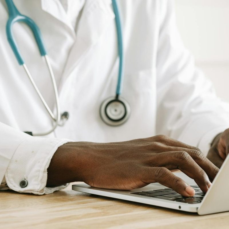Close-up of a doctor using a laptop, wearing a stethoscope and white coat.