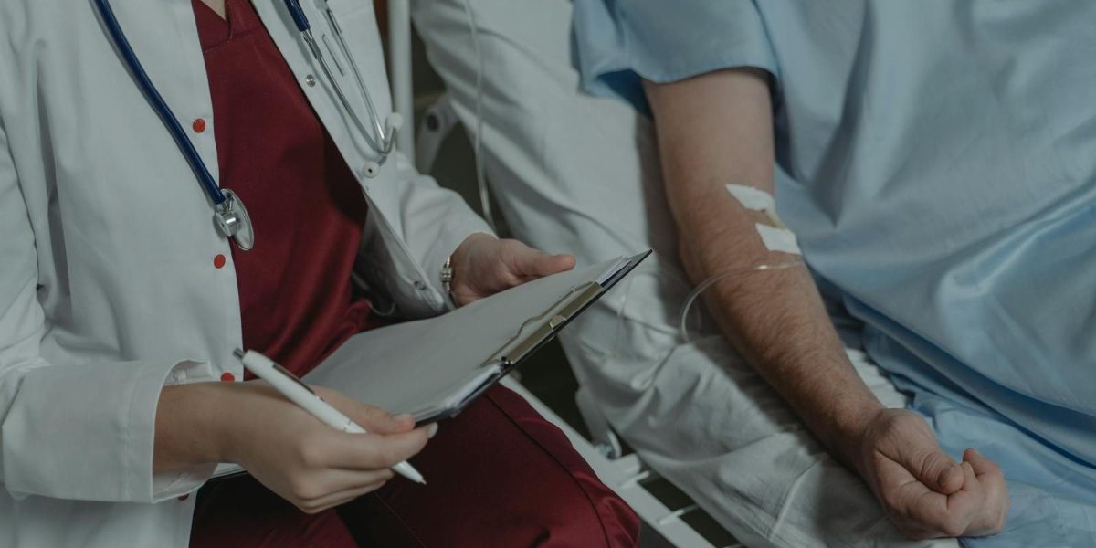 Doctor reviewing medical chart while assisting a patient in a hospital bed.