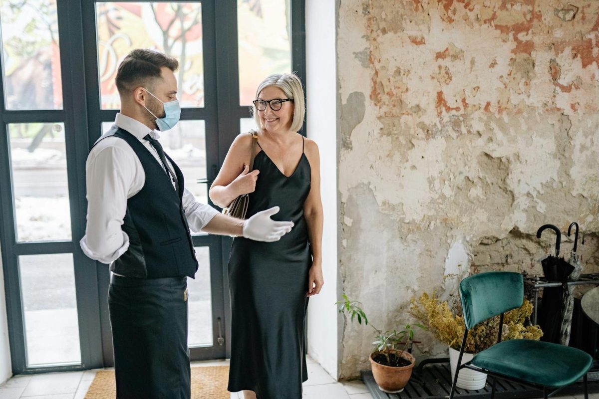 A friendly waiter welcomes a smiling woman in a stylish setting with rustic decor.